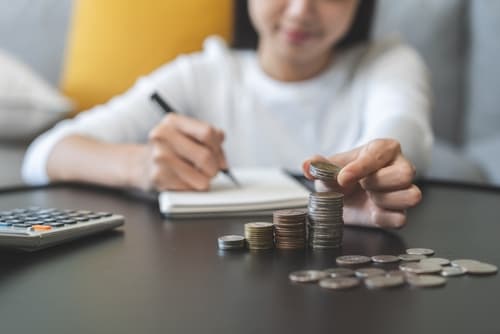Financial,,Asian,Young,Woman,,Girl,Putting,Stack,Coins,On,Table Person counting coins and budgeting with a calculator, representing cost-effective planning for AED cabinets and defibrillator maintenance